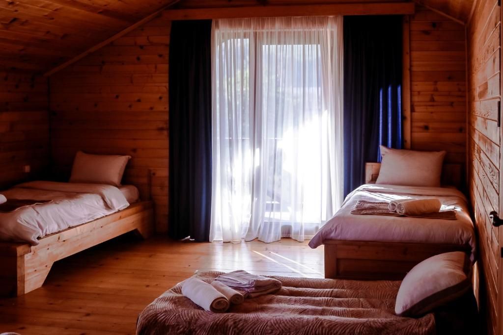 A cozy wooden cabin with two beds, a large window with sheer curtains, and a wooden floor.