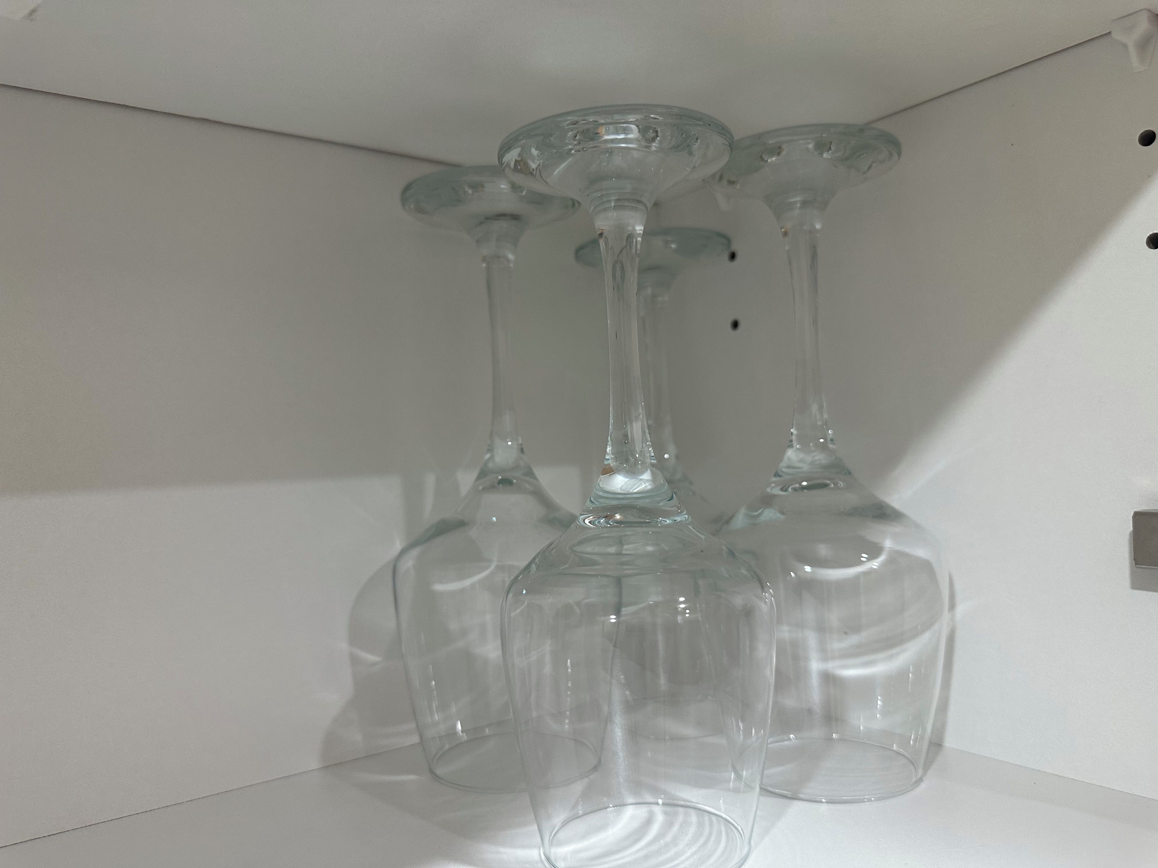 Trois verres à vin en verre transparent, empilés sur une surface blanche, devant un mur uni.