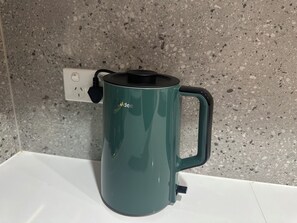 Ein türkisfarbener Wasserkocher mit schwarzem Griff auf einer weißen Arbeitsplatte.