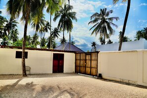 A gated outdoor area with a gravel ground, a metal chair, and a building with a corrugated metal roof. - Exclusive 3-Bedroom Beachfront Villa with Private Pool in Zanzibar (Zanzibar)