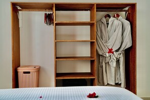 A wooden wardrobe with multiple shelves and hanging space, a wicker laundry basket, and a bed with a white bedspread. - Exclusive 3-Bedroom Beachfront Villa with Private Pool in Zanzibar (Zanzibar)
