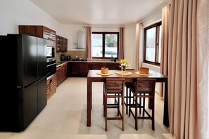 A modern kitchen with a black refrigerator, wooden cabinets, and a dining area with a table and chairs. - Exclusive 3-Bedroom Beachfront Villa with Private Pool in Zanzibar (Zanzibar)