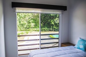 A bedroom with a large sliding glass door leading to a pool area. - Halani Beach House - Ciudad del Mar - King bed (Jaco, Ciudad del Mar)