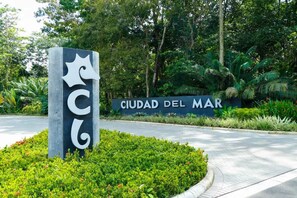A sign for Ciudad Del Mar with a large 'C' logo and lush greenery in the background. - Halani Beach House - Ciudad del Mar - King bed (Jaco, Ciudad del Mar)