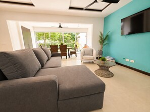 Ein modernes Wohnzimmer mit einer Eckcouch, einem runden Couchtisch und einem Flachbildfernseher, der an einer Türkiswand angebracht ist.