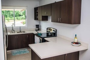 A modern kitchen with dark wooden cabinets, a white countertop, a stove, and a coffee maker. - Halani Beach House - Ciudad del Mar - King bed (Jaco, Ciudad del Mar)