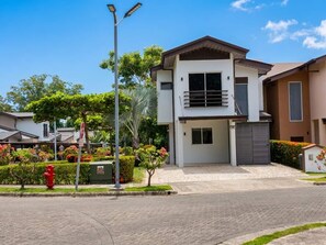 A modern two-story house with a flat roof, a garage, and a well-maintained garden with various plants and a red fire hydrant. - Halani Beach House - Ciudad del Mar - King bed (Jaco, Ciudad del Mar)