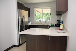 A modern kitchen with a central island, stainless steel appliances, and a window providing natural light. - Halani Beach House - Ciudad del Mar - King bed (Jaco, Ciudad del Mar)