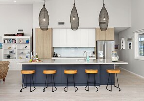 Una cucina moderna con isola centrale, sgabelli da bar, illuminazione a sospensione e vista sul mare.