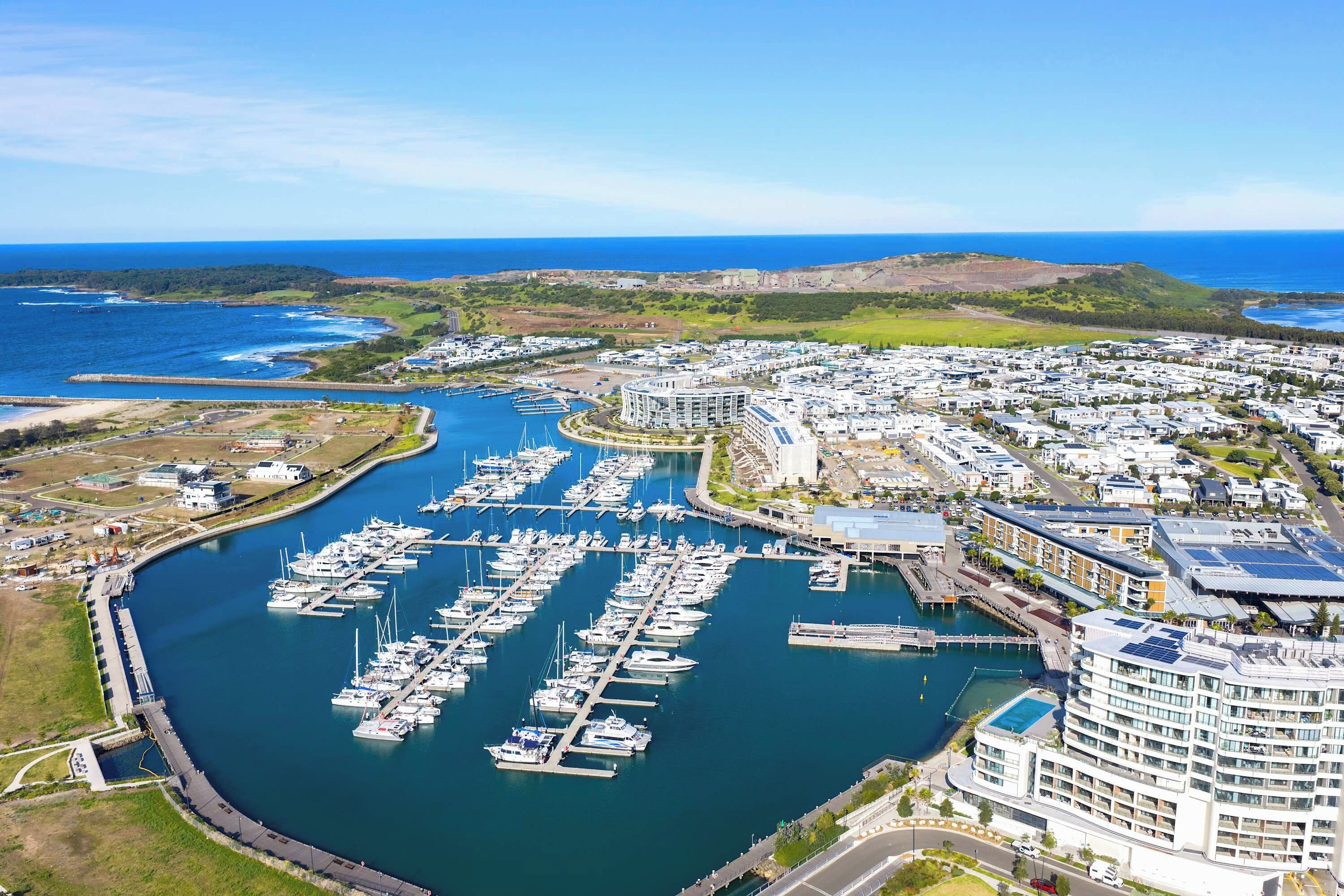 Marina con numerosas embarcaciones amarradas, rodeada de edificios residenciales y un paisaje montañoso.