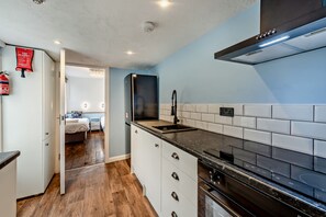Una cocina compacta con armarios blancos, una estufa negra y una pared azul.