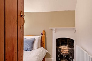 Un dormitorio con cama de madera, pared blanca y chimenea.
