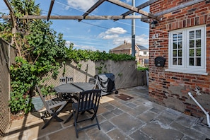 Un patio con mesa y sillas, una parrilla cubierta y un muro de ladrillo con una ventana.