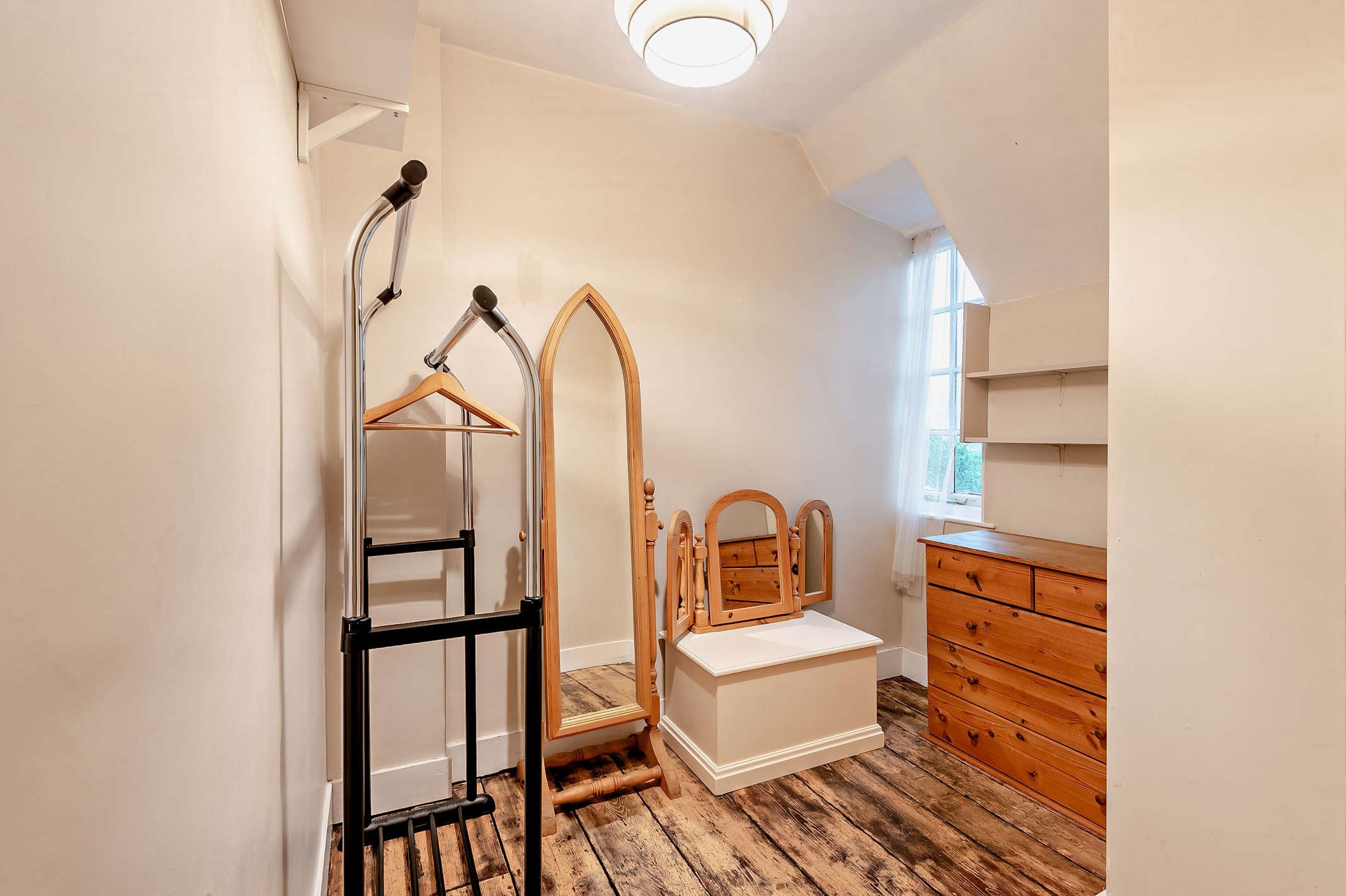 Een kamer met een houten dressoir, een spiegel, een houten stoel en een metalen rek met een houten kapstok.