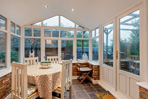 A conservatory with a table and chairs, a stone bench, and large windows.