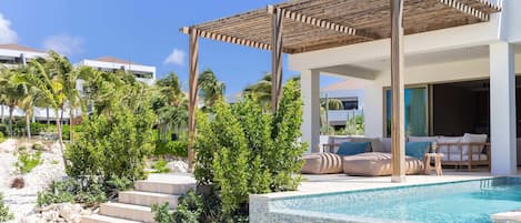 Ein moderner Poolbereich im Freien mit einer Pergola, Stufen zum Pool und einer Lounge mit einer Couch und Kissen.