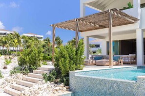 A modern outdoor pool area with a pergola, steps leading to a pool, and a lounge area with a sofa and cushions. - Dolce Vita - Tropical Poolside Paradise (Sint Michiel)