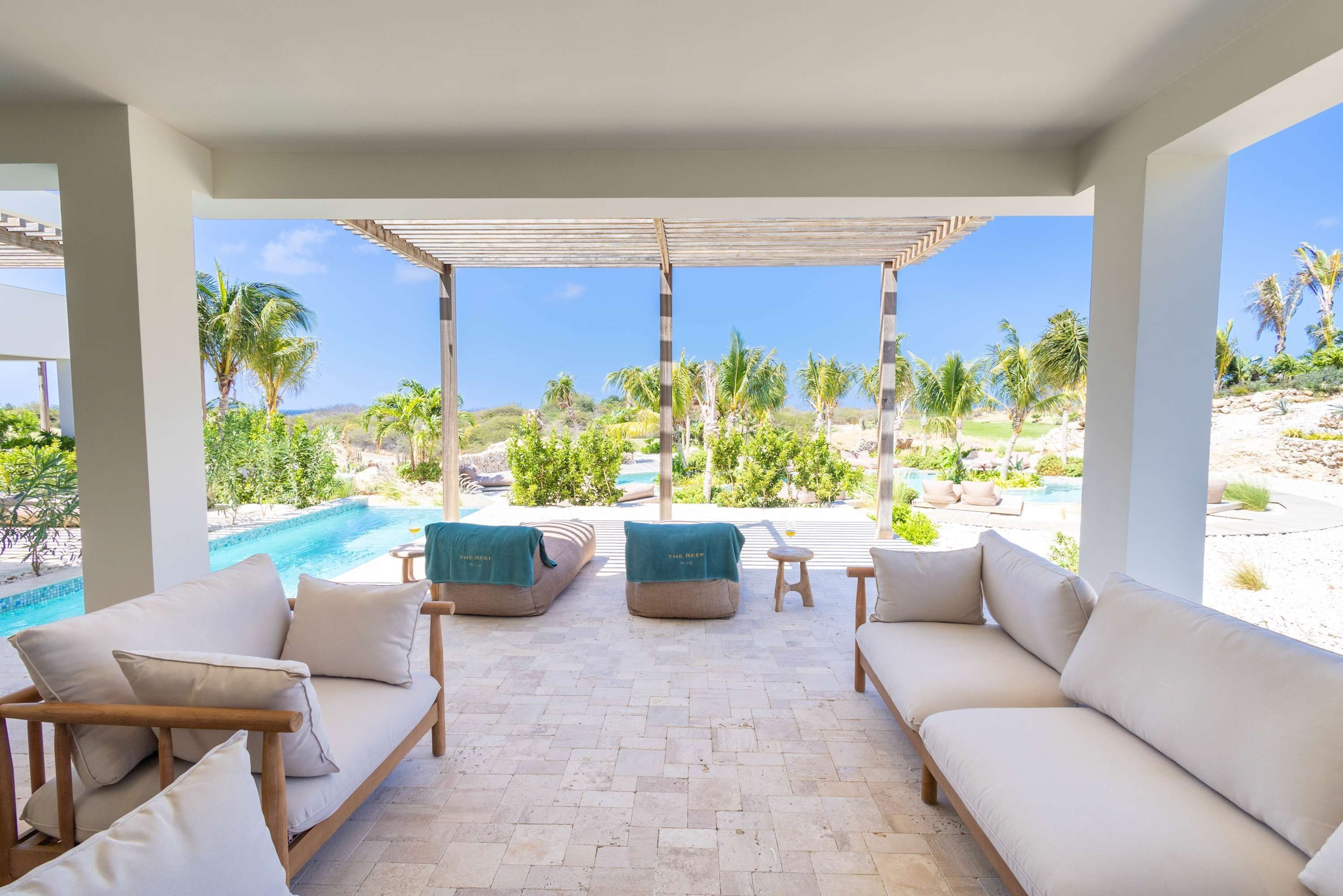 A covered outdoor seating area with a pool view, featuring sofas and a small table.