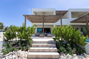A modern outdoor area with a stone staircase leading to a covered seating area, surrounded by greenery and a pool. - Dolce Vita - Tropical Poolside Paradise (Sint Michiel)