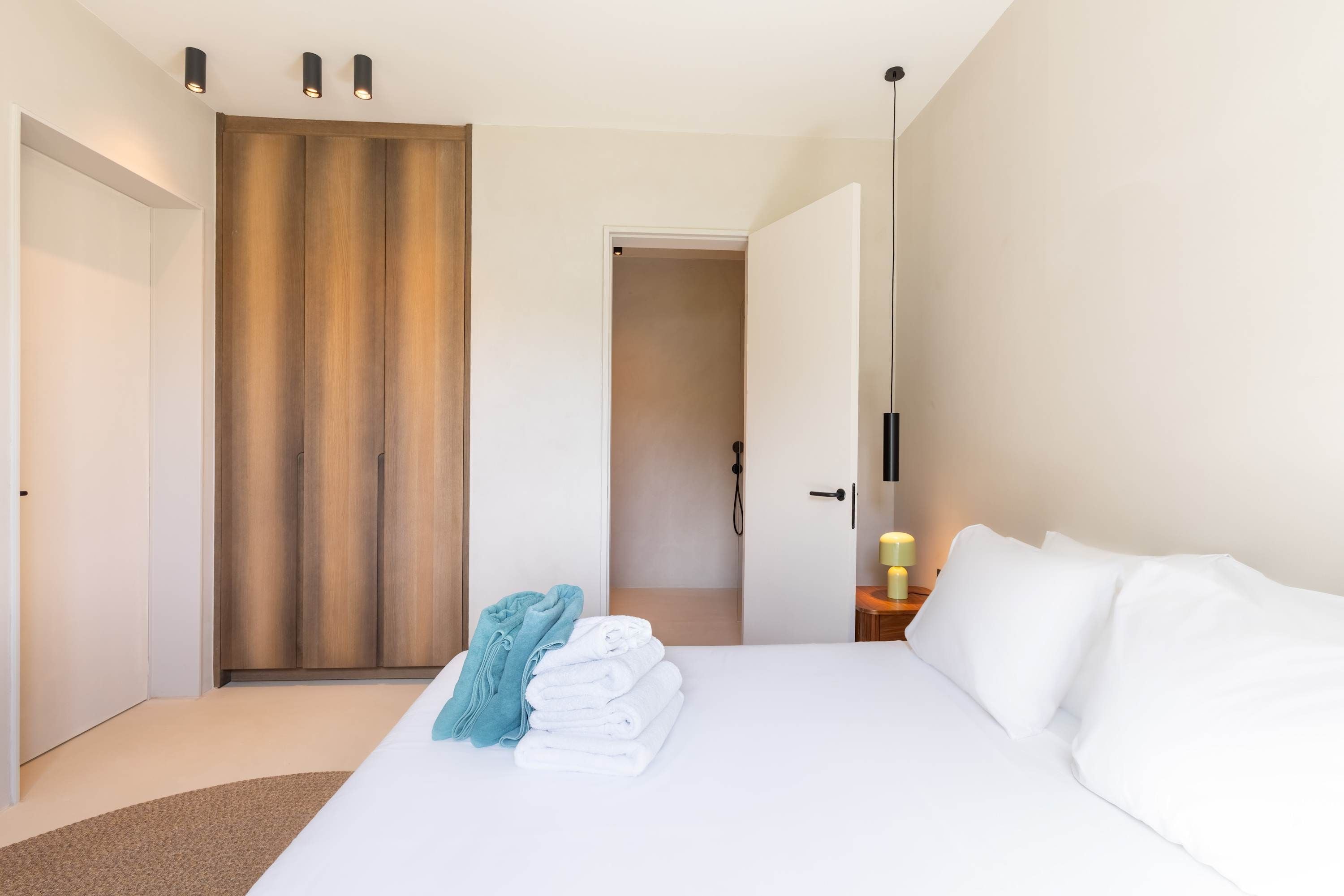 Ein Hotelzimmer mit Bett, Holzschrank, Badezimmer und Nachttisch mit Lampe.
