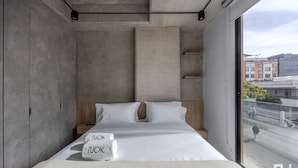 Un dormitorio moderno con una cama grande, dos almohadas, una mesita de noche y vistas a la ciudad a través de una ventana.