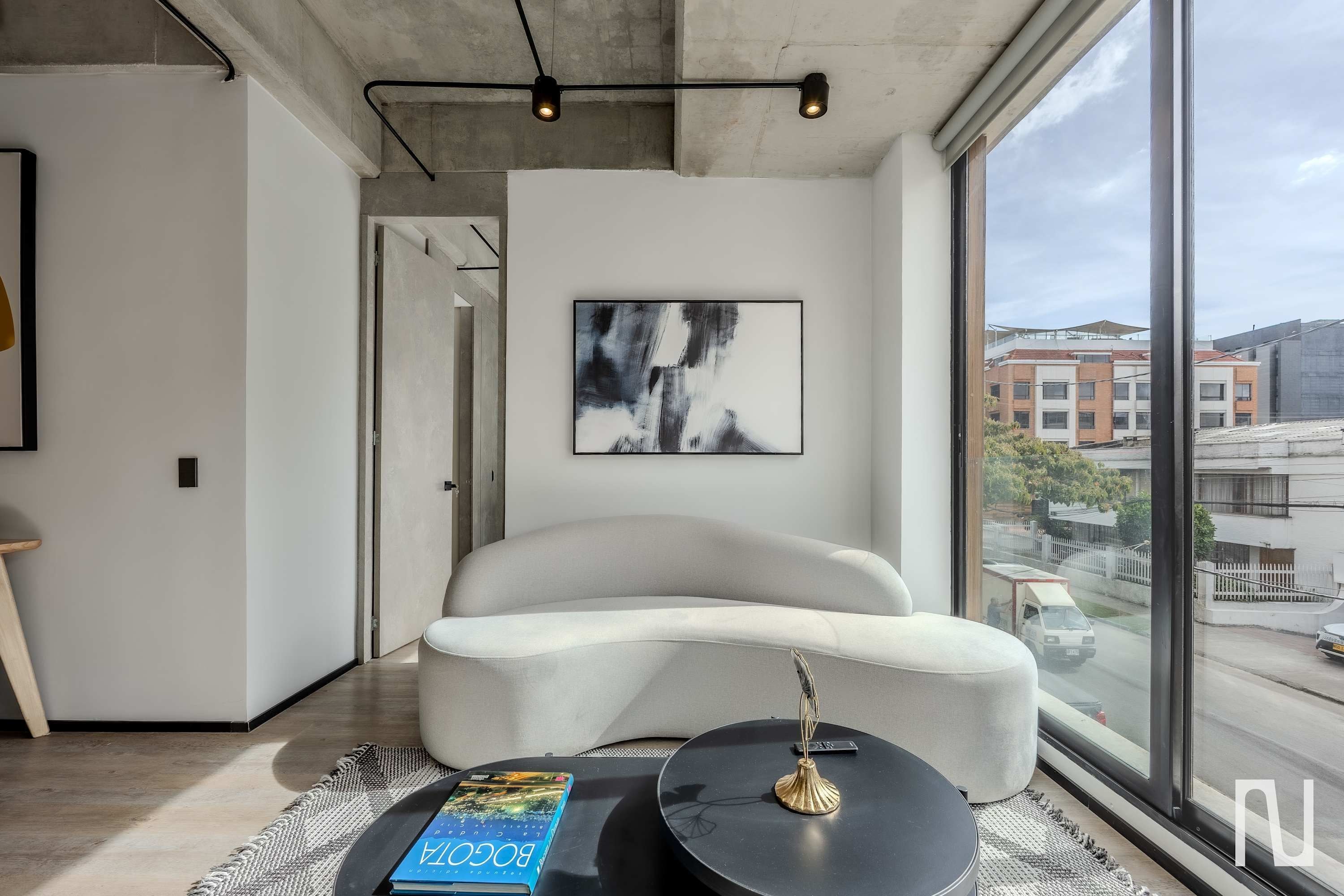 Un salon moderne avec une grande fenêtre, un canapé blanc, une table basse ronde et un lampadaire noir.