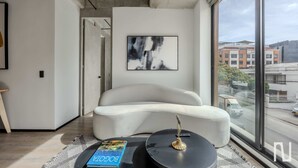 Una sala de estar moderna con un ventanal grande, un sofá blanco, una mesa de centro redonda y una lámpara de pie negra.