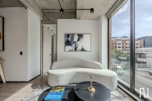 Ein modernes Wohnzimmer mit großem Fenster, einem weißen Sofa, einem runden Couchtisch und einer schwarzen Stehlampe.