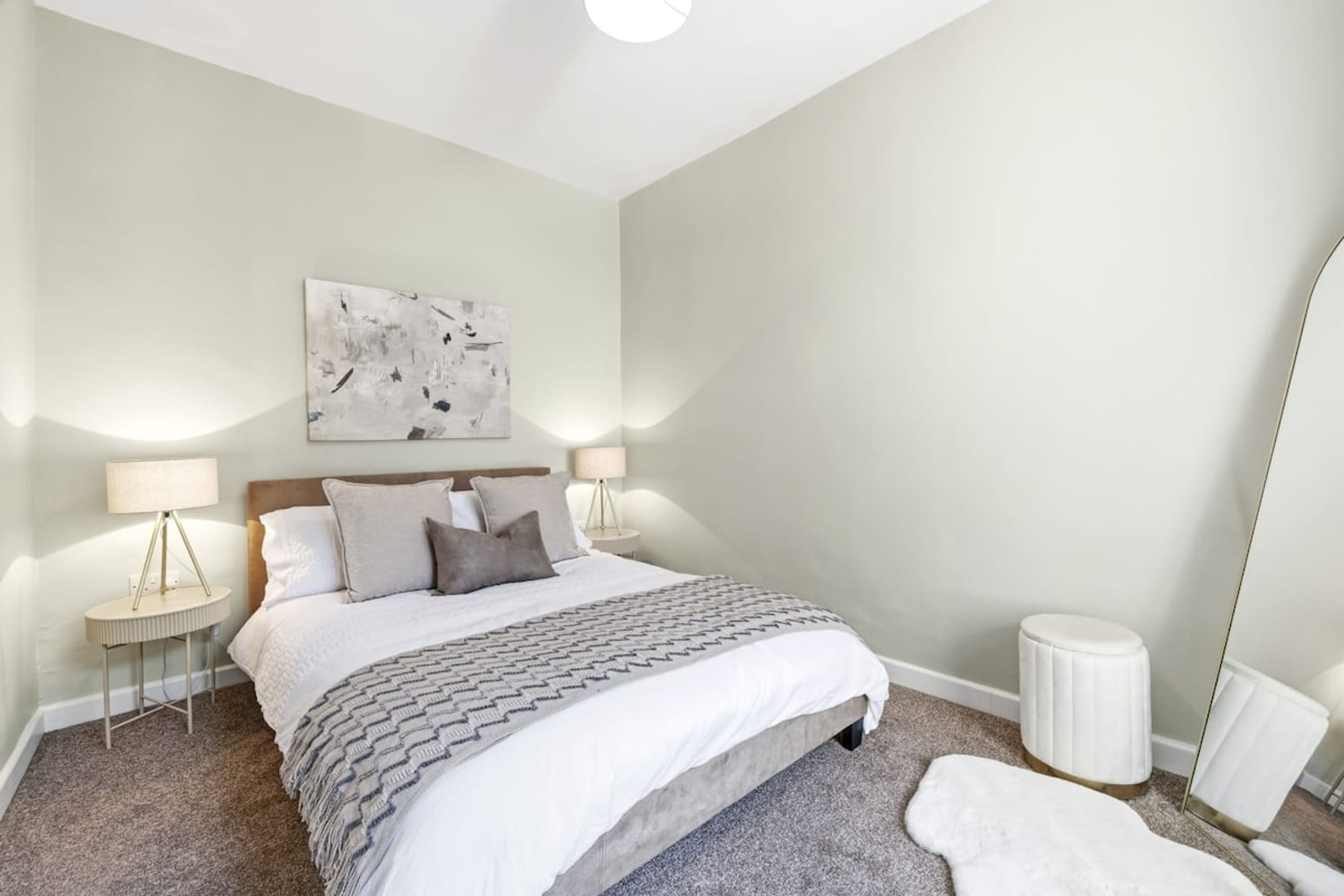 Une chambre à coucher comprenant un lit, deux tables de chevet, une commode, un miroir et un tableau abstrait accroché au mur.