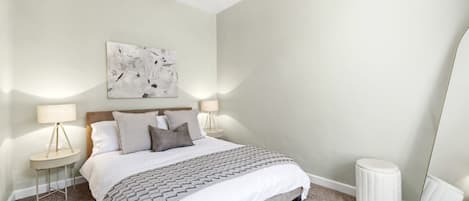 Une chambre à coucher comprenant un lit, deux tables de chevet, une commode, un miroir et un tableau abstrait accroché au mur.