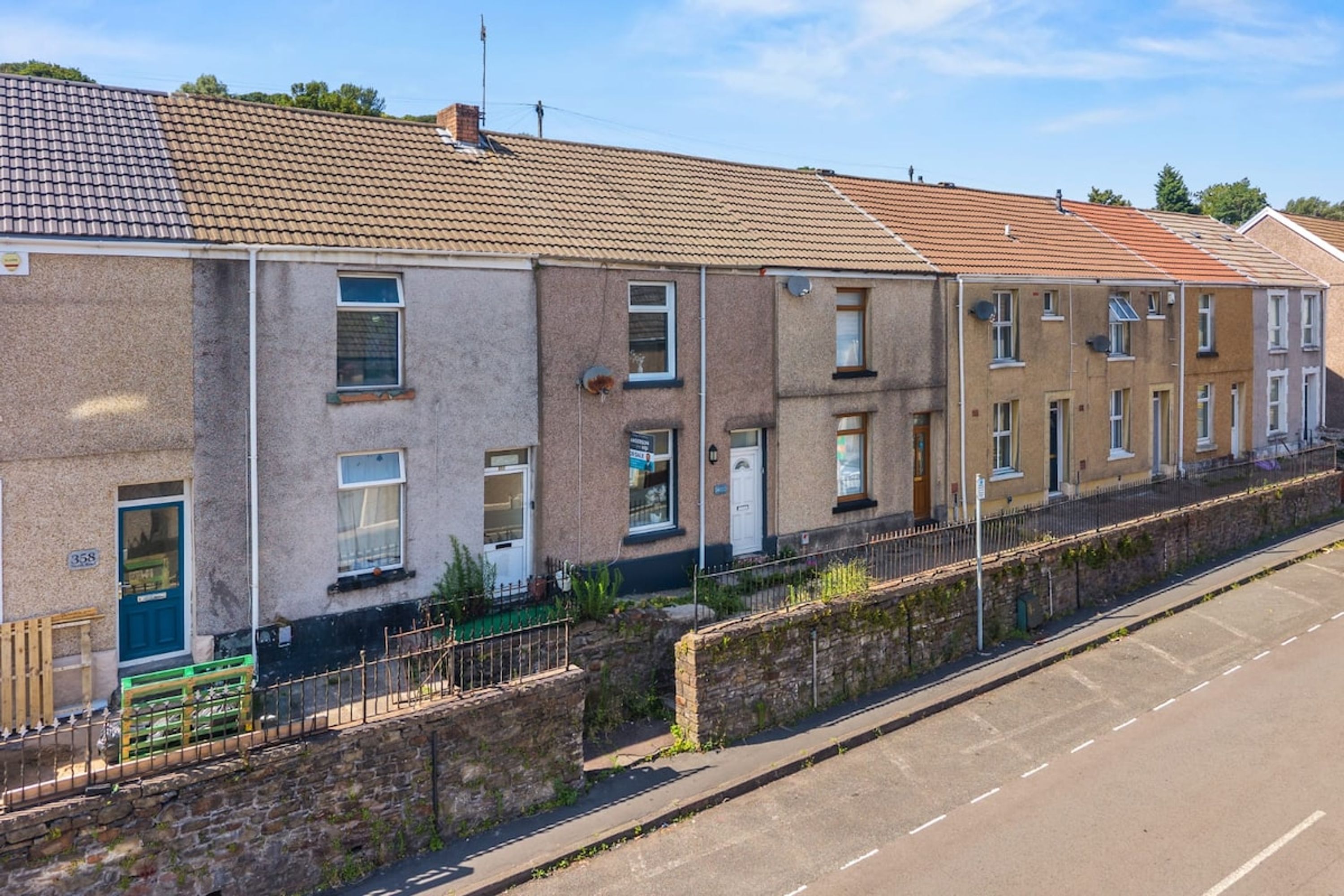 A row of terraced houses with a paved driveway and a stone wall.