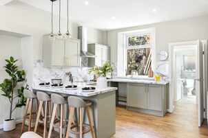 A modern kitchen with a marble countertop, bar stools, and a large window.