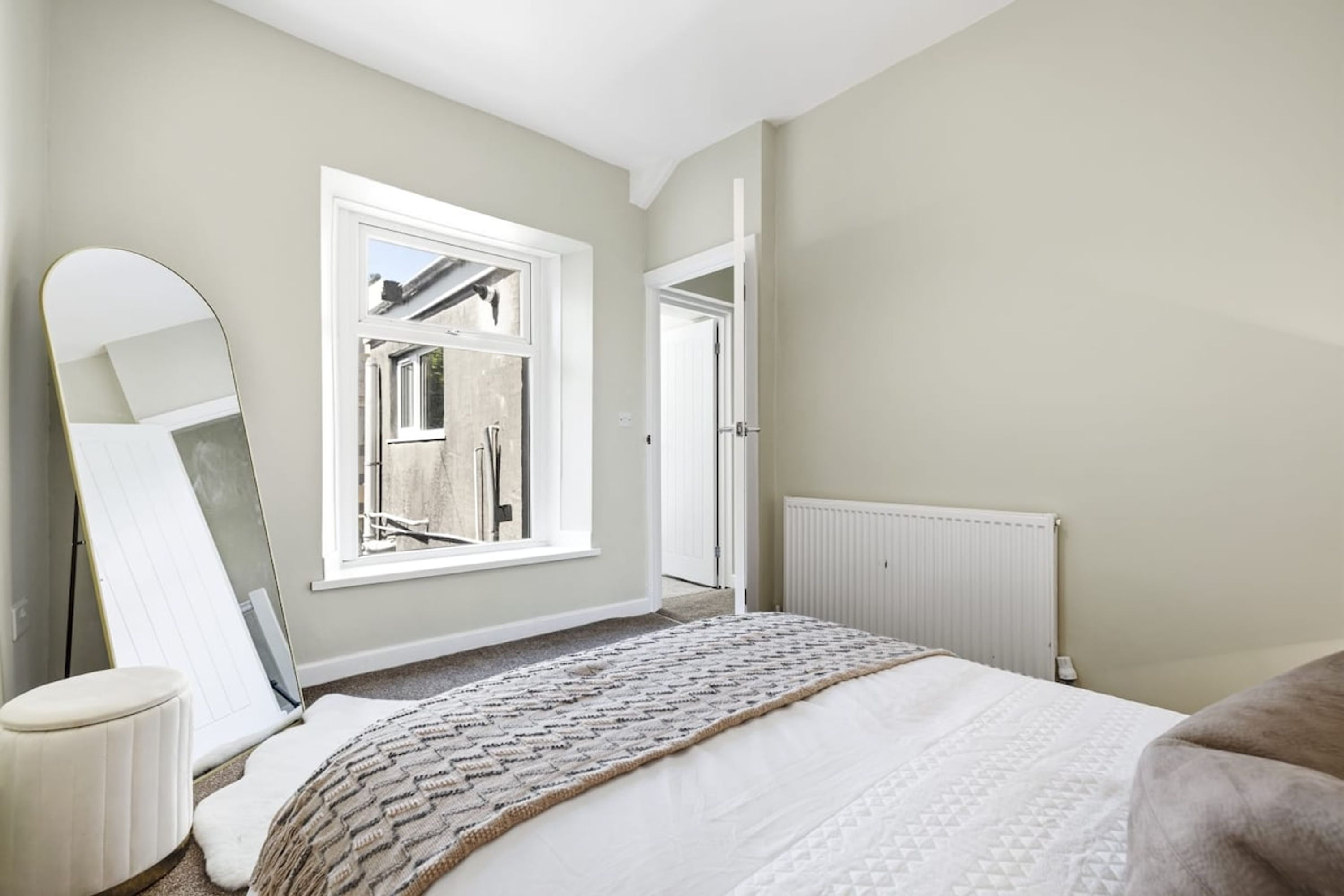Een slaapkamer met een groot bed, een raam, een radiator en een deur.