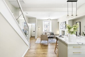 Una cocina moderna con encimera de mármol, un comedor con sofá y mesa de centro, y una escalera que sube a otro nivel.