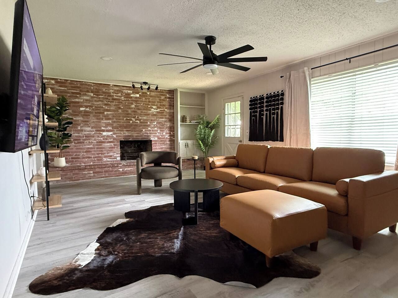 A living room with a leather sofa, a coffee table, a TV, a fireplace, and a brick wall.