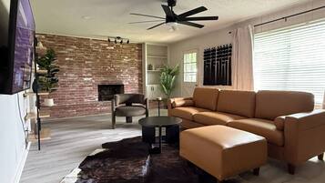 A living room with a leather sofa, a coffee table, a TV, a fireplace, and a brick wall.