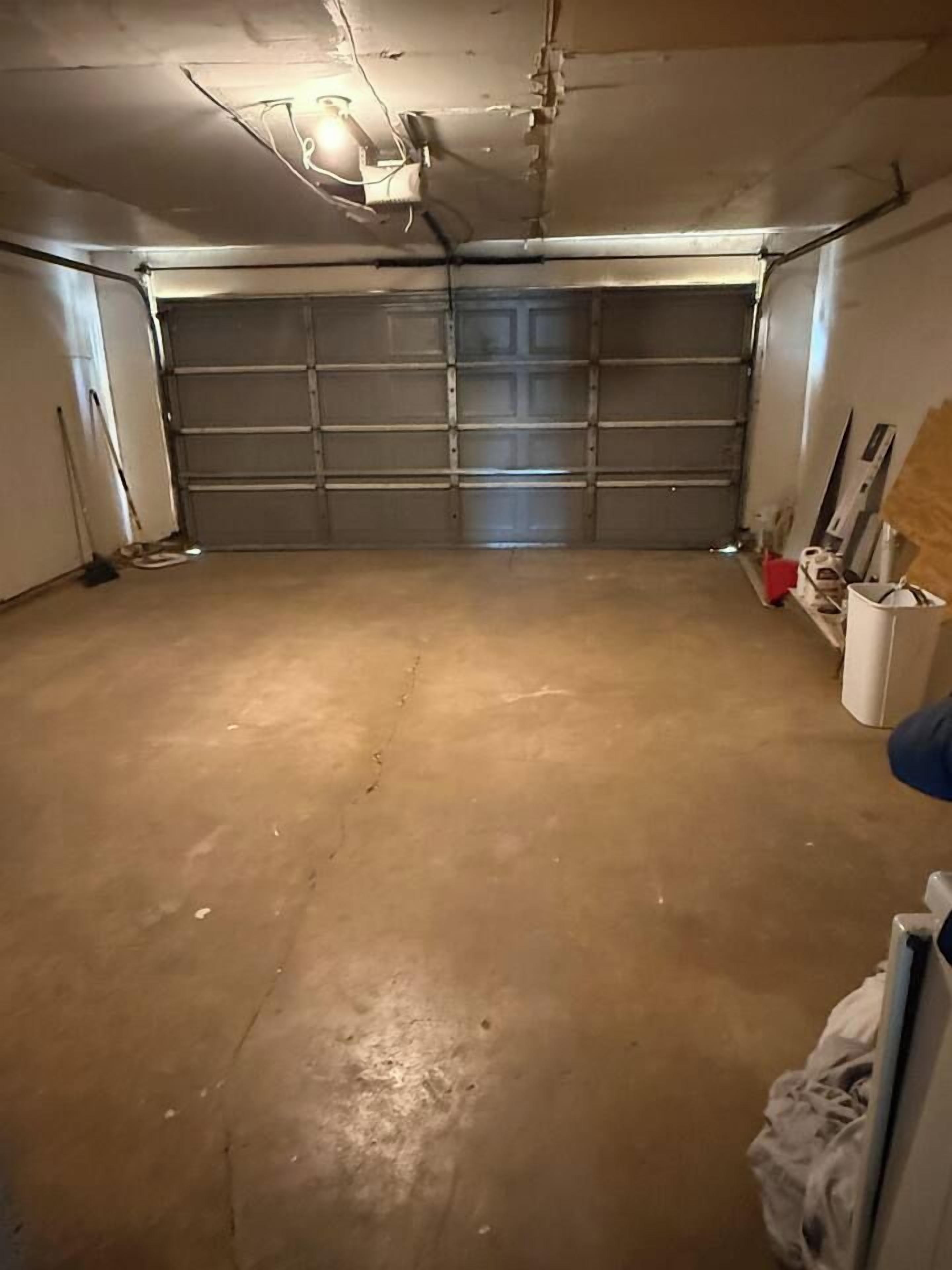 Eine Garage mit Betonboden, geschlossenem Garagentor und einer Deckenleuchte.