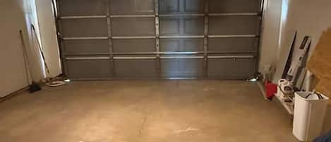Eine Garage mit Betonboden, geschlossenem Garagentor und einer Deckenleuchte.