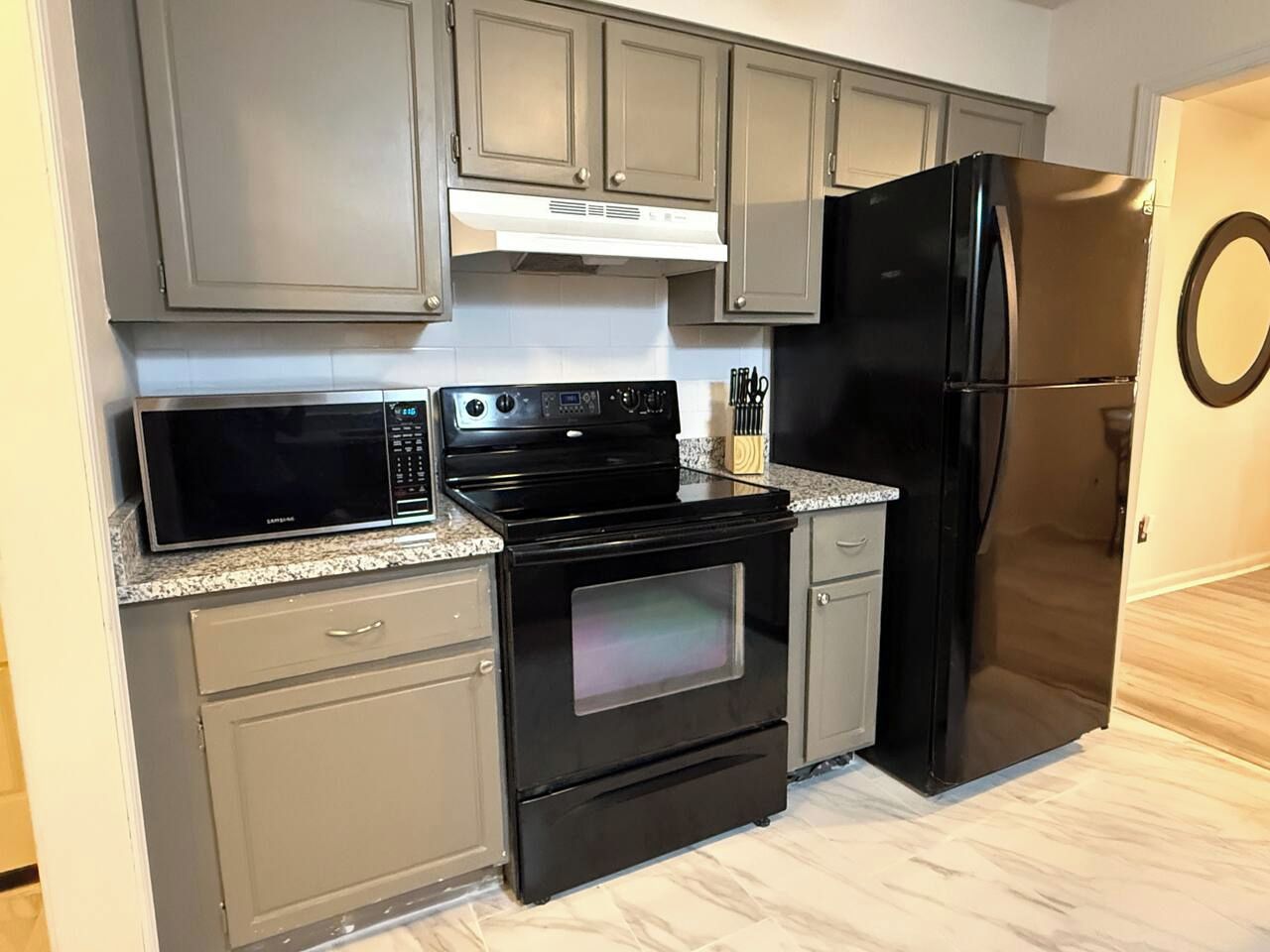 A kitchen with a black stove, microwave, and refrigerator, grey cabinets, and a white countertop.