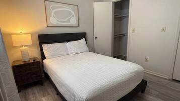 A bedroom with a bed, a nightstand, a lamp, a closet, and a wall-mounted artwork.