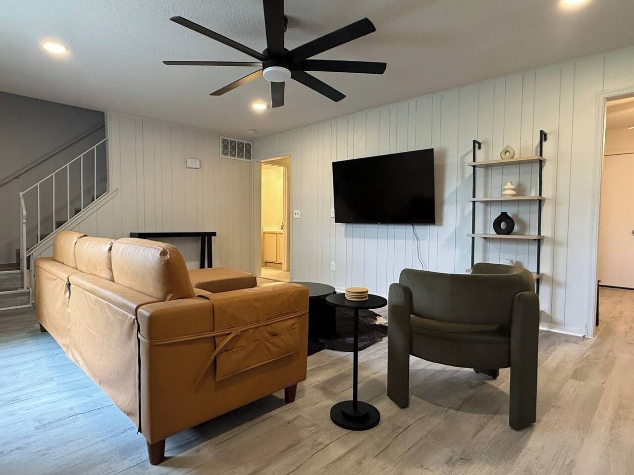 A living room with a sofa, armchair, TV, and a ceiling fan.