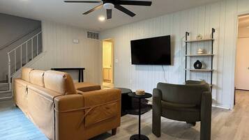 A living room with a sofa, armchair, TV, and a ceiling fan.