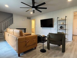 Sala de estar com sofá, poltrona, televisão e ventilador de teto.
