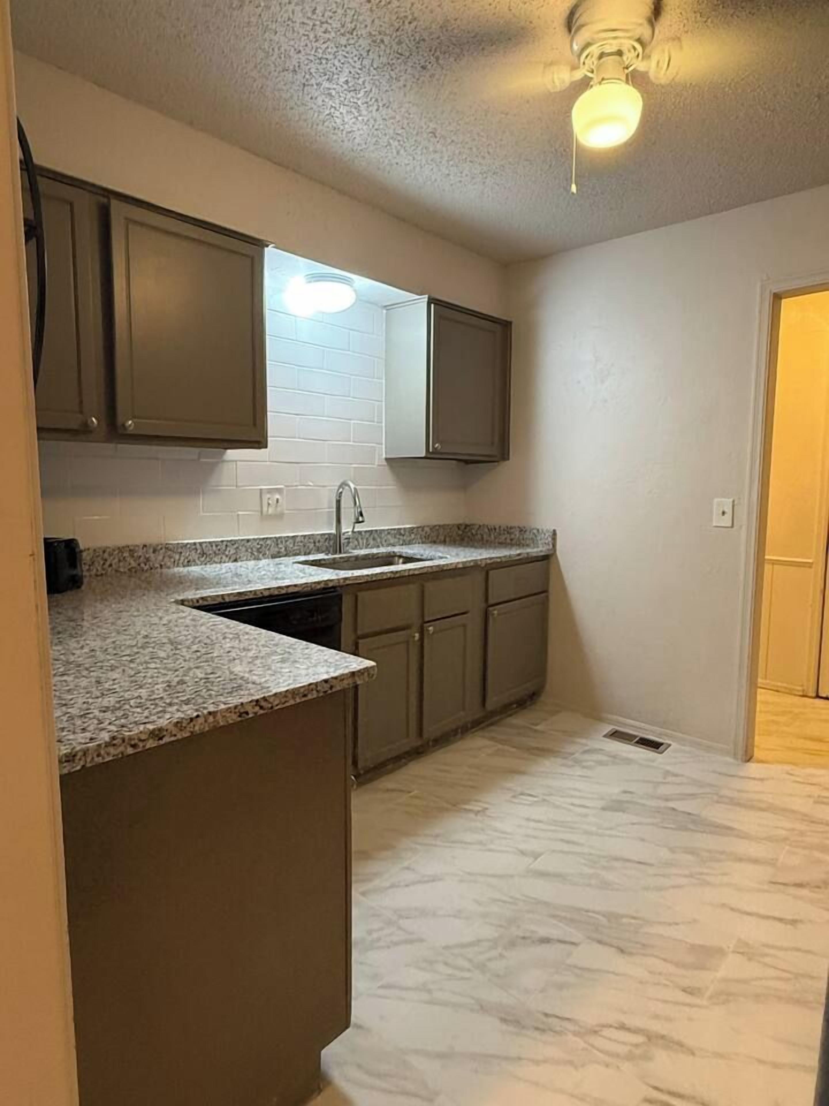 A compact kitchen with granite countertops, a built-in sink, and a ceiling fan.