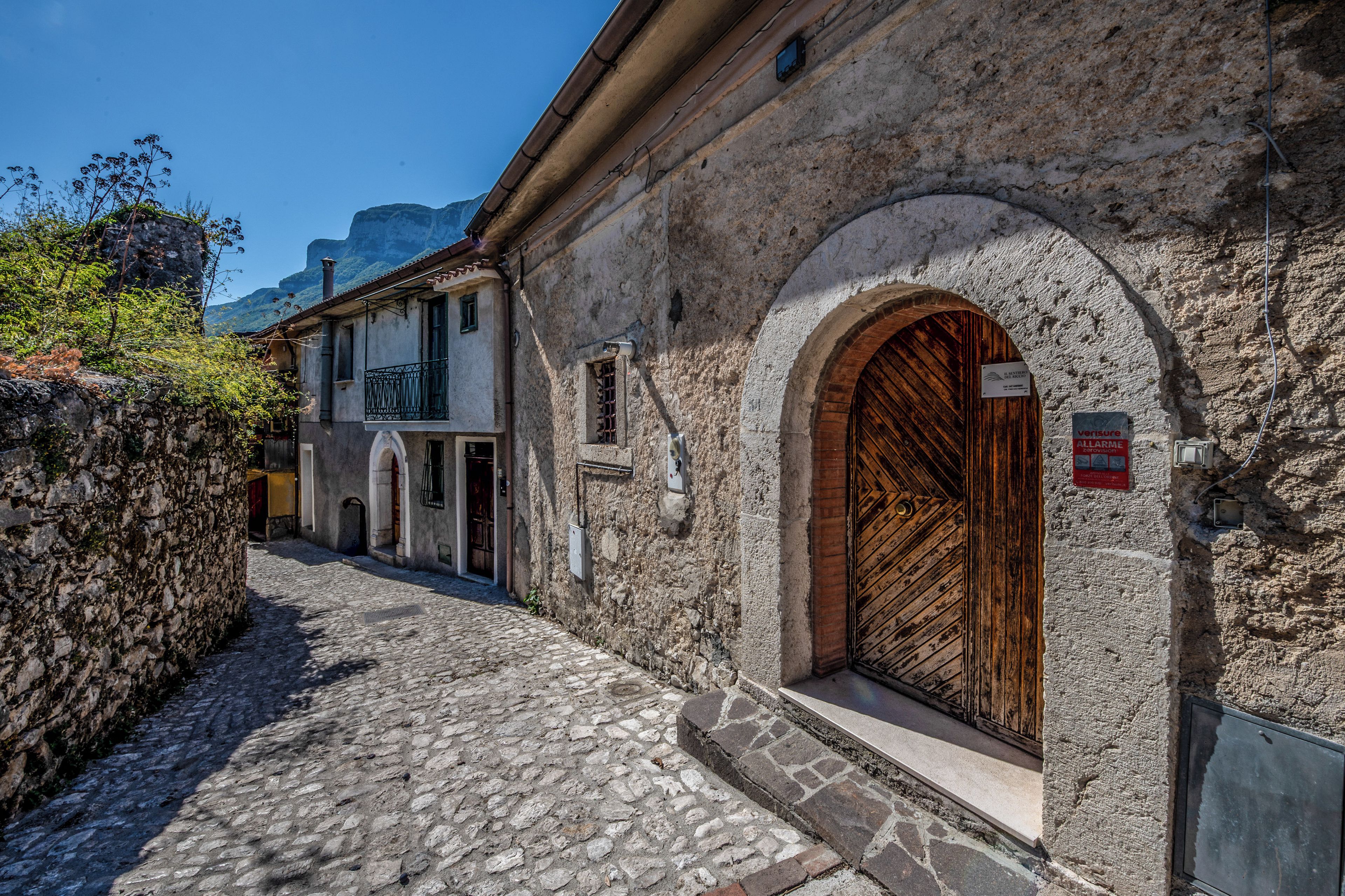A cobblestone street with historic stone buildings, a wooden door, and a sign indicating a fire alarm system.