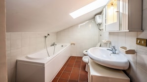 A modern bathroom with a bathtub, toilet, and sink, featuring white fixtures and a sloped ceiling with skylight. - Il Sentiero del Riccio (Sicignano degli Alburni)