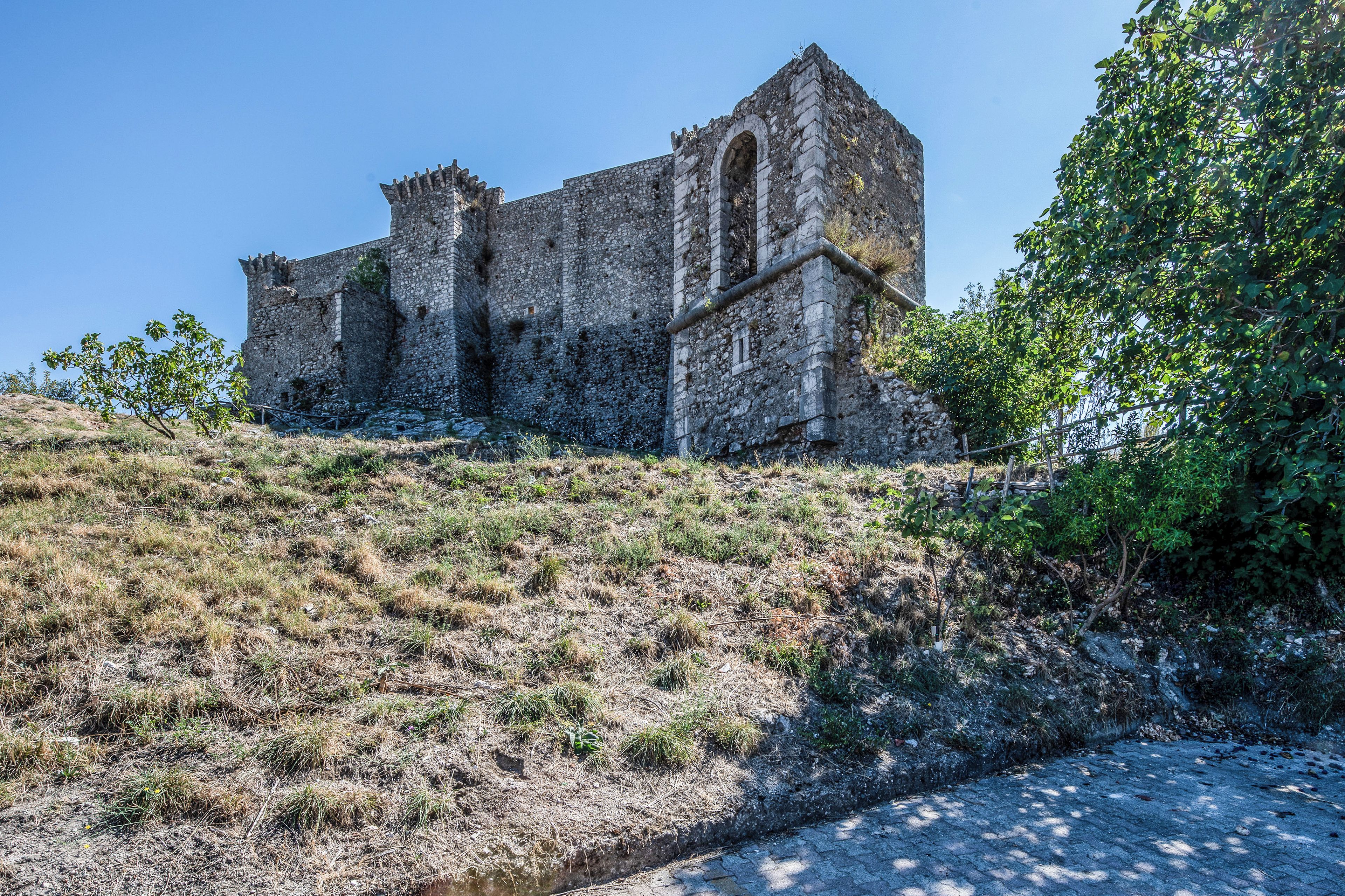 Un ancien bâtiment en pierre, doté de fenêtres en arc de cercle et surplombant une colline abrupte et verdoyante.