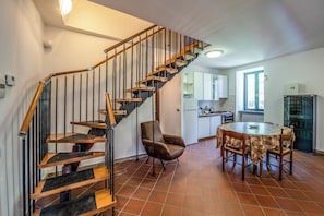 A modern kitchen with a dining area, a wooden staircase, and a chair.