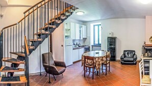 A spacious living area with a wooden staircase, a dining table with chairs, a kitchen in the background, and a fireplace. - Il Sentiero del Riccio (Sicignano degli Alburni)