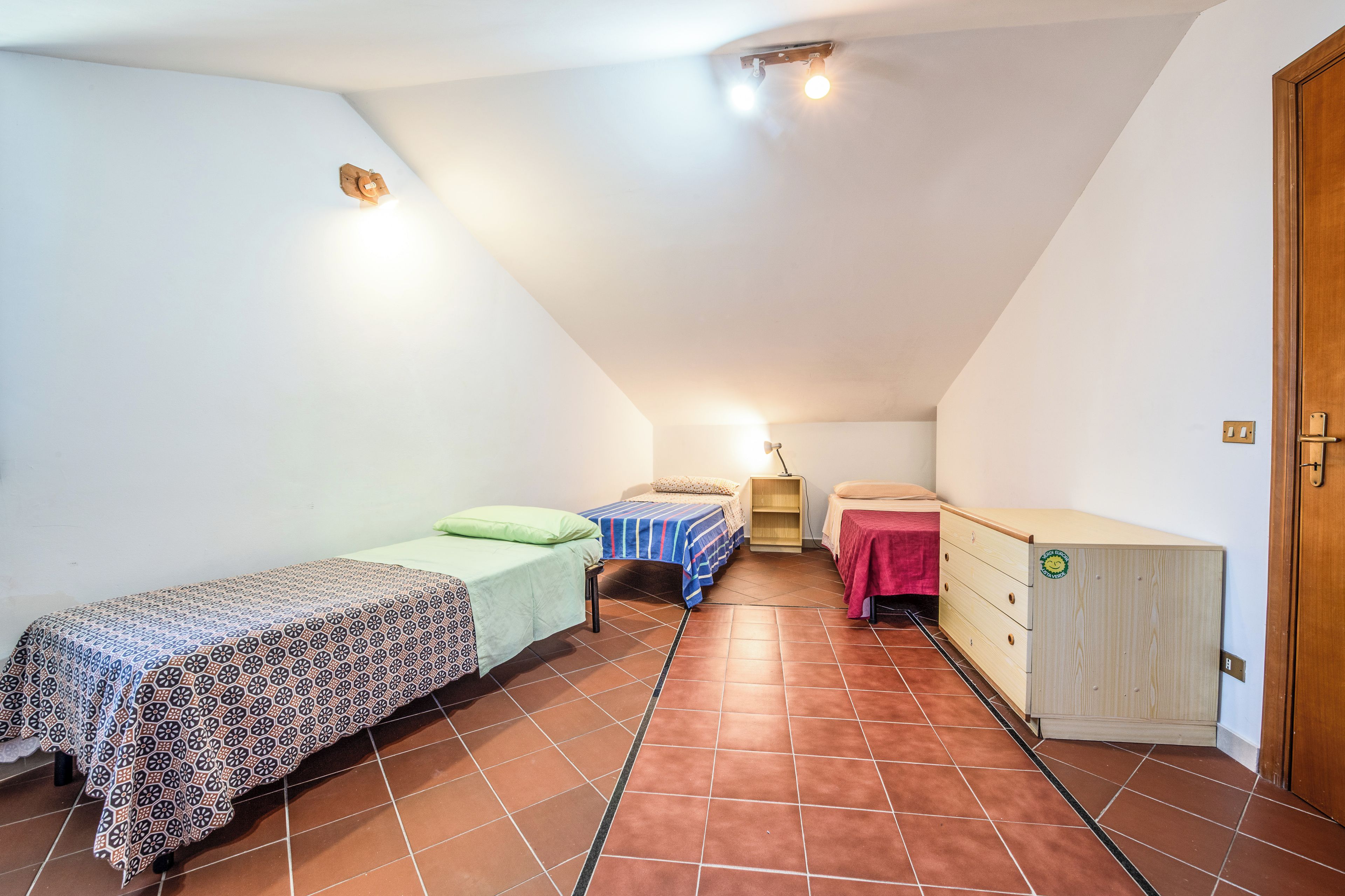 A small, well-lit attic bedroom with two beds, a dresser, and a door.